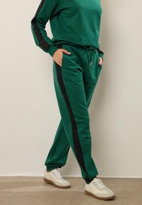 Grön sweatshirt och matchande joggers med svarta sidsömmar; tillverkade av mjukt material; har fickor och dragsko i midjan.