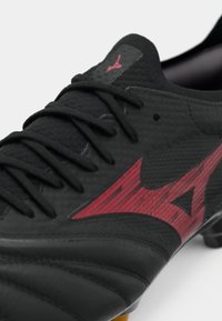 Černé fotbalové kopačky s červeným logem a černými šněrovadly na bílém pozadí, ukazující texturované a šité detaily svrchní části.