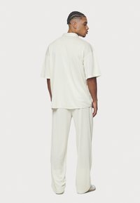 Camisa polo de color beige claro y pantalones sueltos a juego, con una textura suave y mangas cortas, vistos desde atrás.