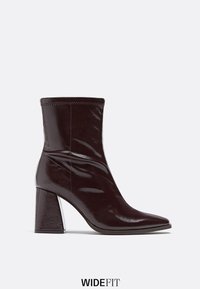 Botte en cuir brun foncé brillant mi-mollet avec bout pointu, talon large carré et surpiqûres visibles sur le bord supérieur.