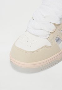 Béžové a bílé tenisky s hladkým koženým svrškem, semišovými detaily, silnými bílými tkaničkami, perforovanou špičkou a světle růžovou gumovou podrážkou.