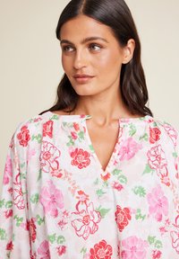 Blomstret bluse i let, teksturert stoff. Har V-hals, samlet skuldre og et fargerikt mønster av rosa, rød og grønne blomster.