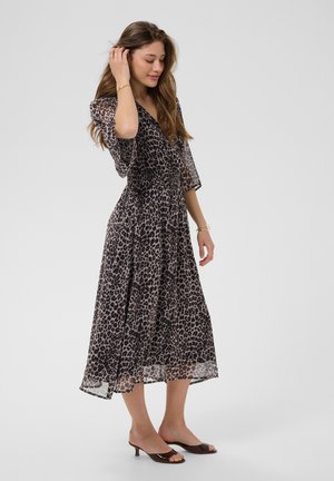 Kobieta pozująca w midi sukience w panterkę z rękawami 3/4 i czarnych otwartych szpilkach kitten heels na jednolitym tle.