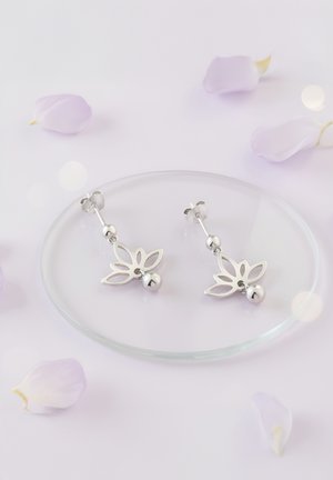 Boucles d'oreilles en argent avec un design découpé en fleurs et des accents de perles rondes, présentées sur une assiette en verre entourée de pétales pâles.
