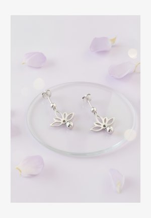 Orecchini d'argento con un design a intaglio floreale, arricchiti da perline tonde, esposti su un piatto di vetro circondato da petali chiari.