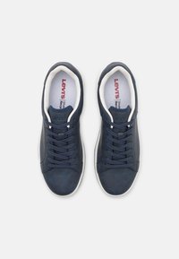 Mornarske plave tenisice s glatkom kožnom teksturom, okruglim vrhom, bijelim gumenim đonom i plavim vezicama. "Levi's" logo vidljiv na ulošcima.
