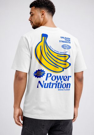 Man wearing a white T-shirt with a large yellow banana graphic and blue text promoting banana-flavored energy bar "Power Nutrition" on the back.
