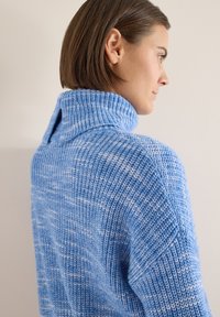 Pull bleu tricoté avec un col montant et une fente au dos. Il présente un motif texturé avec des accents bleu plus clair sur l'ensemble.