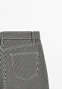 Il tessuto a righe bianche e nere presenta un alto punto vita e una tasca sul retro con cuciture visibili. La texture è liscia e simile al cotone.