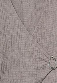 Gros plan d'un tissu gris texturé avec un design enveloppant et une boucle argentée irrégulière sur un côté.
