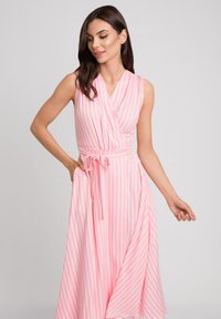 Różowa sukienka w stylu wrap z pionowymi białymi paskami, bez rękawów, z dekoltem w serek oraz wiązaniem w talii. Miękka, lejąca tkanina z delikatnym opadaniem.