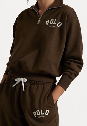 Sudadera marrón y pantalones a juego con logos blancos de "Polo Ralph Lauren", cremallera en la parte superior y cordón blanco en los pantalones.