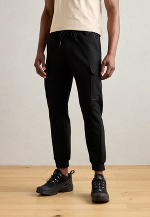 Black athletic joggers with a drawstring waist, two side pockets, and elastic cuffs, paired with black sneakers.