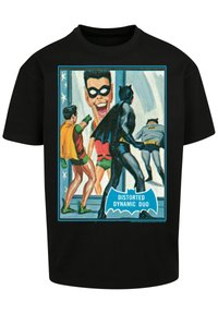 Juodas medvilninis marškinėliai su spalvingu grafikiniu atvaizdu, vaizduojančiu du superherojus, su tekstu „IŠKREIPTAS DINAMINIS DUETAS“ mėlyname šikšnosparnio formos fone.