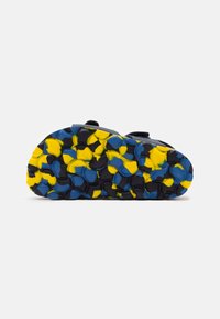 Suela de sandalia negra con un patrón texturizado en colores azul, amarillo y negro, diseñada para ofrecer agarre y tracción.