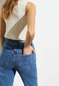 Avskuren, beige, ribbad linne med vertikala ränder som kombineras med högmidjade, blå jeans i denim med lapplommer.