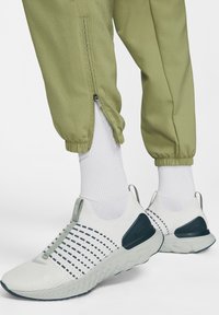 Chaussures de sport blanches et bleu marine avec une tige en mesh texturé, une semelle plate et des accents verts, associées à un pantalon de jogging vert clair à jambes fuselées et des chaussettes blanches.