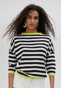Black and white striped sweater with a round neon green neckline and hem. Features three-quarter sleeves and a front pocket detail.