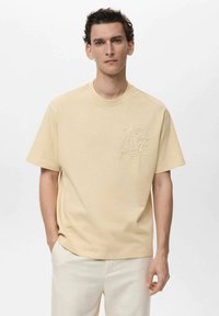 Tricou scurt, bej, din bumbac, cu un design embosat cu palmier pe partea stângă a pieptului și croi lejer.