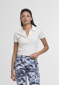 Hvit kortermet polo med spiss krage og en halv-knapp placket, kombinert med blå kamuflasje cargo-bukser med sidelommer.