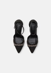 Escarpins noirs en suédine végan à bout pointu, ornés d'une lanière métallique tressée décorative sur le devant et d'une bride à la cheville.