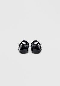 Sandálias de couro preto envernizado com tiras ajustáveis, sola plana e design de bico arredondado. Estilo simples e minimalista, sem padrões visíveis.