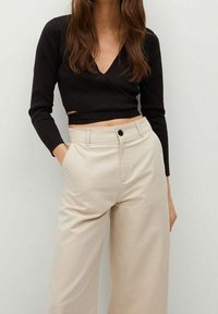 Black wrap top with long sleeves, paired with high-waisted, light beige wide-leg trousers featuring a front button and side pockets.
