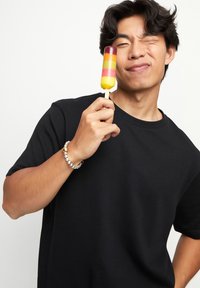 Polochón colorido con capas amarilla, rosa y púrpura en un palo de madera, sostenido por una persona que lleva una camiseta negra y una pulsera de cuentas.