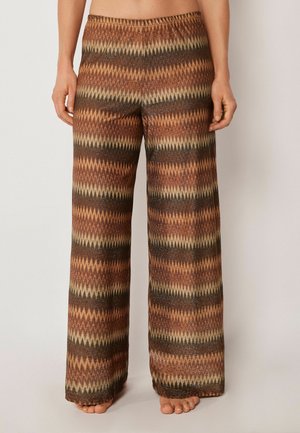 Pantalon à jambes larges avec motif zigzag marron, beige et rouille, porté pieds nus, visible de la taille aux pieds sur un fond uni.
