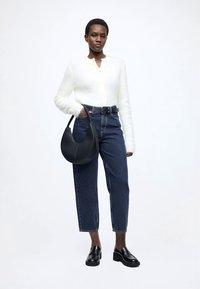 Cardigã branco felpudo, jeans azuis de cintura subida, sapatos de couro pretos e uma mala preta curvada. Design simples e moderno com texturas contrastantes.