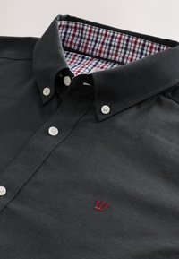 Polo noir à boutons avec doublure intérieure du col à carreaux et petite broderie rouge d'une couronne sur la poitrine.