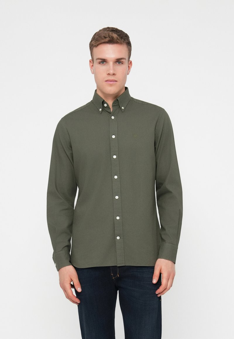 Camisa de manga larga color verde oliva con cuello abotonado, botones blancos y un logo sutil en el pecho. Tejido suave, corte entallado.