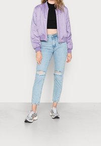 Purple satin bomber jacket with ribbed cuffs, paired with light blue distressed jeans and silver athletic shoes.