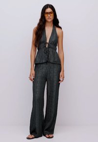 Haut à bretelles vert foncé avec une fermeture à nouer, motif texturé ; associé à un pantalon large dans le même matériau. Grandes lunettes de soleil ambrées.
