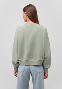 Felpa oversize verde menta con collo e polsini a costine, abbinata a jeans azzurri a vita alta. Tessuto morbido, vestibilità casual.