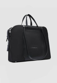 Bolso de cuero negro con doble asa, cierre de cremallera, textura lisa y un bolsillo frontal con logo en relieve. Forma rectangular.