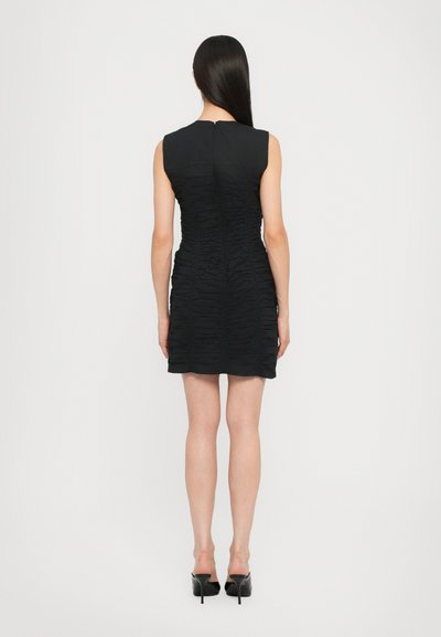 Black sleeveless dress with textured ruched fabric, above-the-knee length, and a hidden back zipper. Paired with black high-heeled shoes.