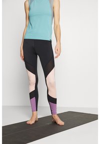 Černé legíny s vzory a růžovými a fialovými akcenty, v kombinaci s světle modrým topem bez rukávů. Materiál vypadá pružně a lehce.