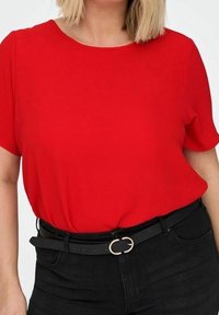 Top corto de manga corta rojo hecho de una tela texturizada, combinado con una cinturilla negra con cinturón que presenta una hebilla circular dorada.