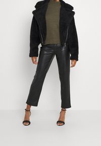 Sort faux fur jakke med krave, lynlås lukning; olivengrøn striktrøje; sorte læderbukser; sorte strop sandaler.