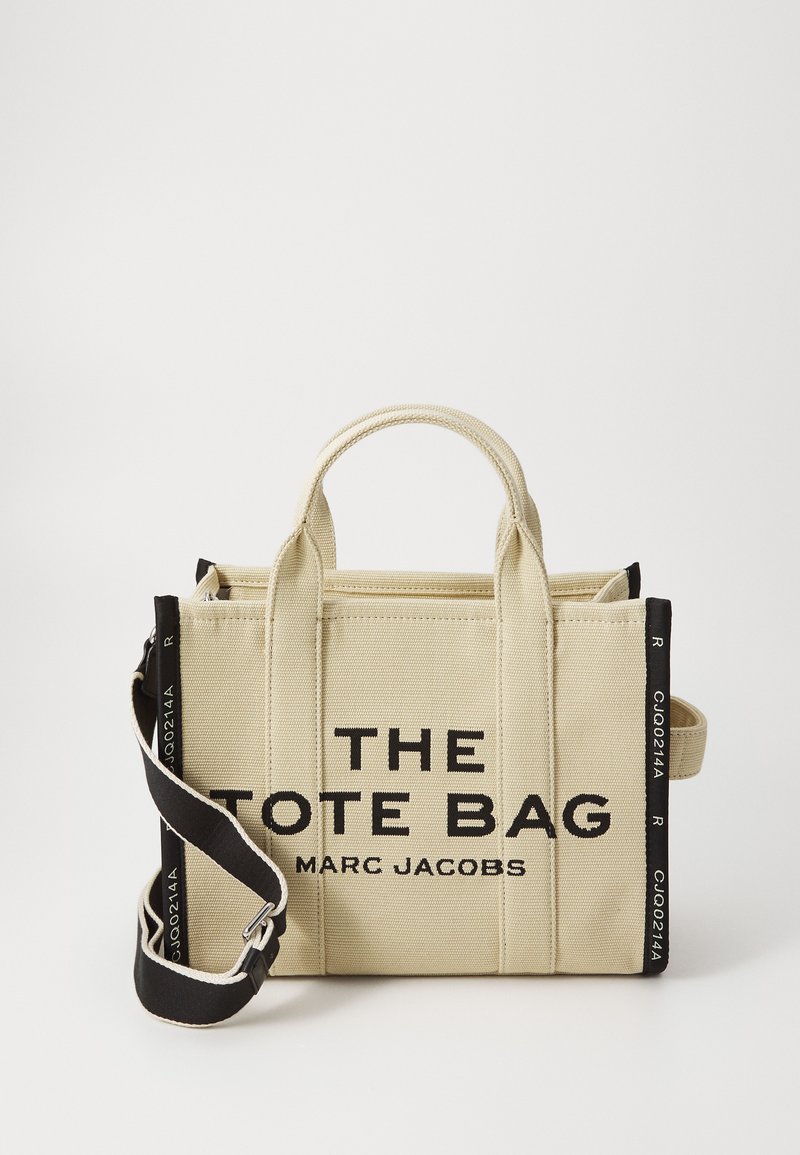 Beżowa torba płótno z czarnym napisem "THE TOTE BAG" i "MARC JACOBS". Posiada podwójne uchwyty oraz odpinany czarny pasek na ramię.