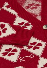 Röd och krämfärgad stickad cardigan med ett diamantmönster som innehåller hjärtan och blommor, ribbade muddar och en detalj med träknapp.