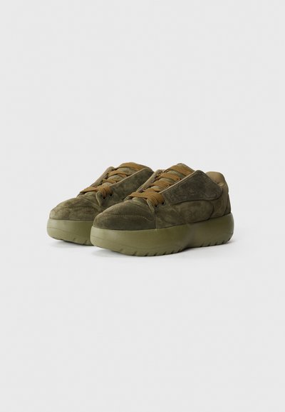 Olive green suede sneakers with a thick rubber sole, round toe, and matching laces. Features cushioned ankle support and textured details.