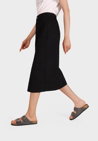 Gonna midi in denim nera con silhouette dritta, tasche anteriori e vita abbottonata, abbinata a sandali grigi slip-on con doppie fibbie.