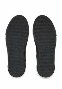 Černé gumové podrážky bot s texturovaným designem, který obsahuje linie a vzory, označené logem "Calvin Klein Jeans". Dvě podrážky zobrazené zeshora.