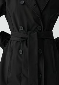 Černý trenčkot z hladké tkaniny, s dvouřadým zapínáním na knoflíky, páskem v pase a kapsami na stranách se klopami.