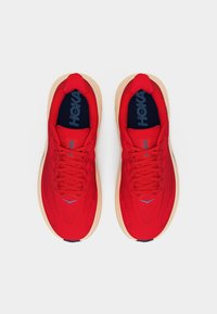 Ζευγάρι κόκκινων παπουτσιών τρεξίματος HOKA με μπεζ σόλες, σε θέα από πάνω, δεμένα και τοποθετημένα δίπλα-δίπλα σε λευκό φόντο.