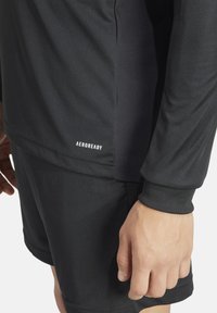 Zwarte Aeroready sportshirt met een gladde, vochtafvoerende textuur, lange mouwen en een getailleerd ontwerp, gecombineerd met bijpassende shorts.