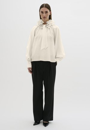 Crème blouse met een gerimpelde kraag en strikdetail, gecombineerd met zwarte high-waisted broek en puntige zwarte schoenen. Gladde stoftextuur.