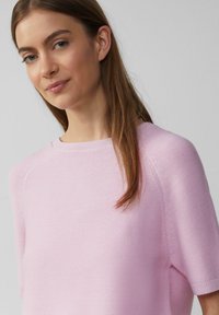 Jasnoróżowy sweter z dzianiny z krótkimi rękawami raglanowymi, okrągłym dekoltem i prążkowaną teksturą, prezentujący gładki, miękki wygląd.